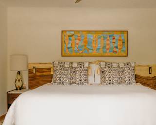A Deluxe Garden View Room bed invites with crisp sheets, cushions in local fabrics and blue and gold wall art of fish above.