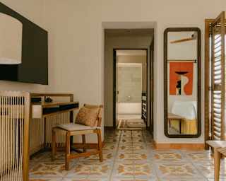 Eye-level view through an Ocean View Suite bedroom, past a desk and a wall mirror either side of a corridor to a bathroom.