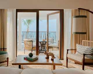 View across the lounge of an Oceanfront Suite through glass doors to the balcony, where comfortable chairs enjoy vast views.