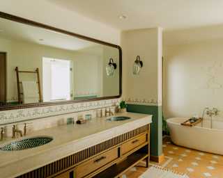 A bath tub rests in an alcove behind a long marble and wood basin unit with a mirror in the serene Wellness Suite bathroom.