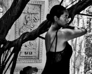 Jack Davison's chiaroscuro image of a woman standing next to a tree near the spa entrance, by a wall with a Mayan carving.