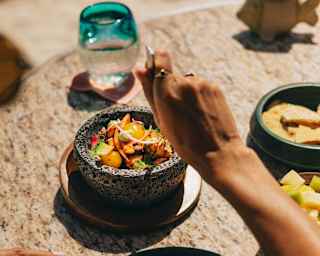 A woman digs her fork into a stoneware bowl of vibrant ceviche, seen over the diner's shoulder at a table at Freddy's Bar.