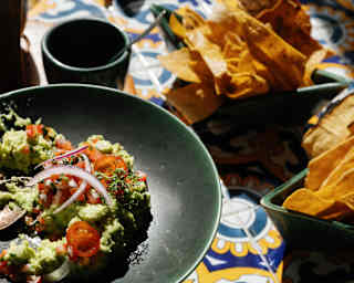 Tomato, onion and avocado salsa with two bowls of tortilla chips create a vibrant lunch on a yellow and blue-tiled table.