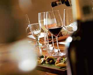 View of a wine tasting table with glasses of red, white and pink, and a dish of nibbles, seen between bottles in soft-focus.