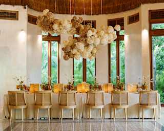 A dining table for twelve is ready for guests beneath decorative hanging pompoms and the high thatched roof of Palapa Tolok.