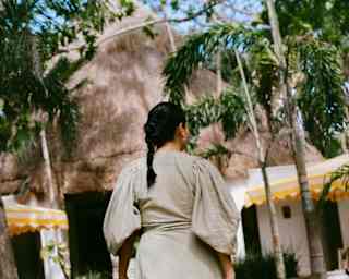 In sage uniform dress, a female member of staff with dark hair in a plait walks towards the hotel lobby, seen from behind.