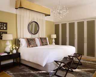 View of a large white Superior Room bed with tapestry cushions and a princess canopy with drapes tucked behind a wall mirror.