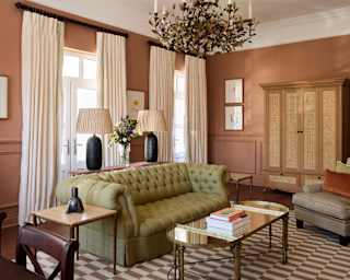A wide olive Chesterfield-style sofa takes centre stage in a Deluxe Suite living room with ornate chandelier and glass table.