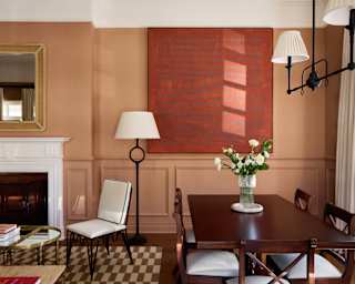 Peach-tone walls envelope the living room of a Deluxe Suite with large abstract wall art, dining table and fireplace area.