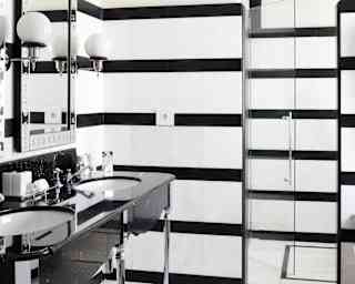 View into a Garden Cottage Suite bathroom with a solid black vanity unit, mirrors and a shower behind monochrome-tiled walls.