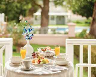 A breakfast table, ready with fruit, juice, pastries and flower vase on the veranda of a Garden Cottage overlooking the pool.