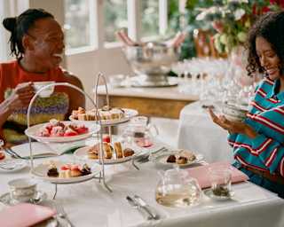 A male and female guest laugh as they raise their cups at an afternoon tea of sweet and savoury delights, served on stands.