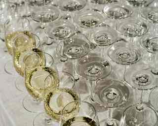A row of glasses of sparkling white wine sits at the front of a table of upturned, unused wineglasses, seen at a celebration.