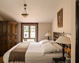 A window with painted a border looks onto rooftops, seen over a bed in a cosy Superior Room with a dark wood corner cabinet.