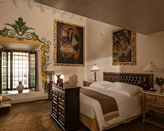 A bay window with illustrated border illuminates a large bed and two giant religious artworks in a Junior Suite with oxygen.