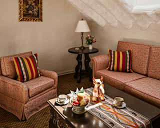 Teacups rest on a table, flanked by a red sofa and chair with stripy cushions, in a cosy corner beneath rendered eave beams.