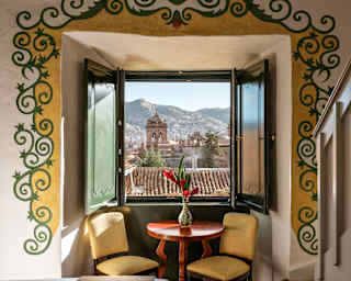In a Junior Suite bay window with an illustrated border, a red table and two yellow chairs enjoy breathtaking rooftop views.