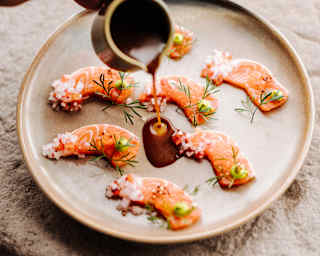 A plate with seven slices of trout, prepared Nikkei style, receives a pouring of Leche de Tigre sauce at Oqre Restaurant.