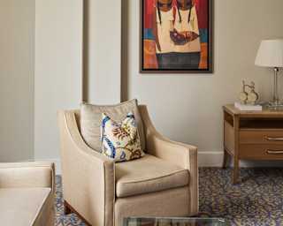 A piece of local art hangs on the wall behind a cream Georgian-style armchair in the lounge area of a Deluxe Junior Suite.