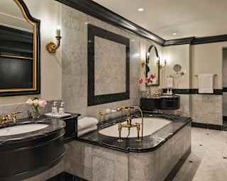 View into the opulent bathroom of a Terrace Suite with grey marbled tiling and black marble sink and bath top with gold taps.