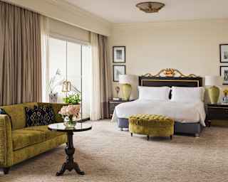In the elegant Terrace Suite, a green velvet sofa and stool marry with gold tones in the black headboard of a wide white bed.