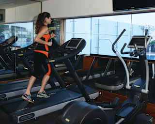 A female guest enjoys using equipment in the hotel gym and fitness room with the pool through the window