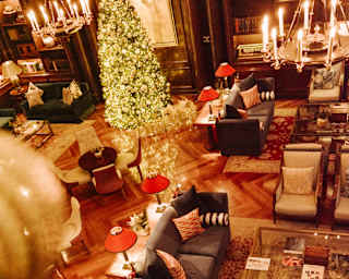 High-angle view of the glowing lobby with sofas, chairs and  Persian-style rugs alongside a resplendent Christmas tree.