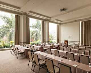 Three tall windows spill light into Salón Park, where ten long beige tables, each seating four chairs, face the front.