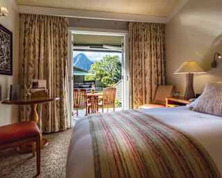 Soft king-size bed in an elegant hotel room with sunny patio seating area beyond
