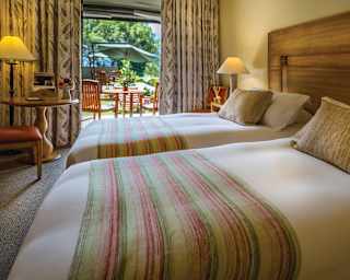 Two soft double beds side-by-side next to open patio doors and outdoor terrace