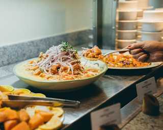 A woman's hand lifts a spoonful of a delicious sauce-covered dish topped with onions from a buffet of other plates.