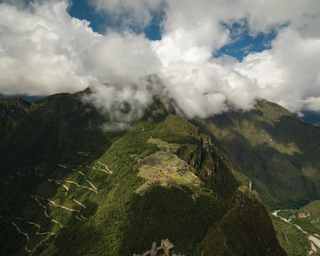 View of cloud-topped Machu Picchu, seen from the top of Huayna Picchu, capturing the winding mountain path and ruins.