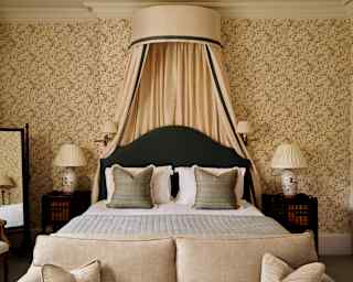View over a sofa to a bed and princess canopy, butter-cream drapes secured behind a black headboard, seen in Botticelli Room.
