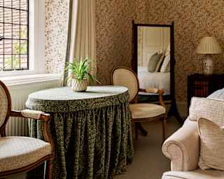 Light from windows falls on a skirted table with a plant in a view of the Botticelli room, with beige, gold and floral hints.