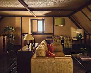 View into Jade's living area with a large bronze sofa and russet cushions, dark wood consoles and a dining table and chairs.