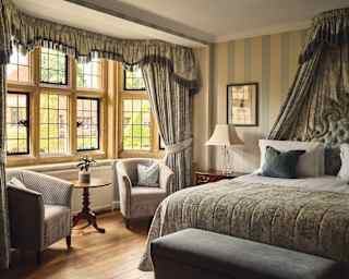 Light from a bay widow illuminates Hyacinth Suite's bed, dressed in greys with eighteenth-century style drapes and headboard.