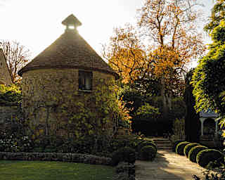 A small window peers out of a cylindrical stone dovecote. The hexagonal peak of the conical tiled roof replaced with glass