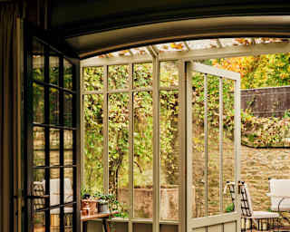 Large sage-framed doors open to a private walled terrace, seen from the Artichoke Suite interior through a glasshouse area.