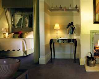 A fire roars in an old fireplace flanked by brass coal scuttle and hearth tidy. On the chimney breast is a painting of nudes