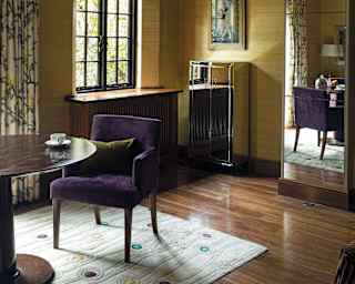 Blue and white floral curtains and roman blinds dress windows. A dining chair in purple upholstery sits at a polished table
