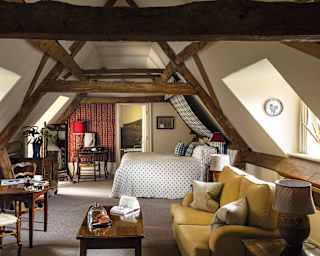 A-frame exposed vintage beams lend a barn-like quality to this room, furnished with antiques and blue, yellow and red fabrics
