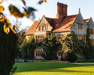 Stunning image of Le Manoir, clad with wisteria, brushed with gold sun and set in emerald lawn, viewed through autumn leaves.