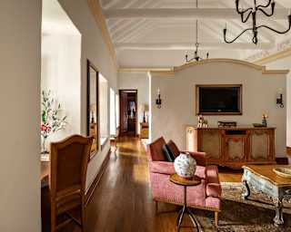View down a polished wood corridor passing an open lounge with antique furniture, to a room beyond in a One Bedroom Suite.