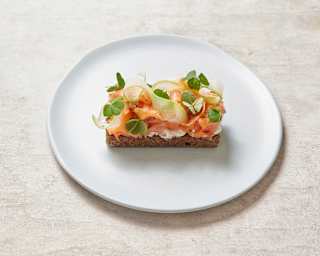 A traditional chapla bread with trout, shaved olluco and citrus, served on a simple white plate on a pale-painted table.