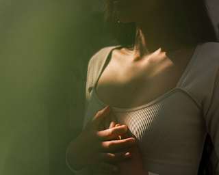 A woman in a white crop top, seen from the neck down, holds her hands over her solar plexus during breathwork at Hypnôze Spa.
