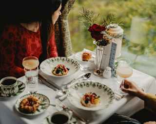 Two guests gaze through the window at an Afternoon Tea in the Cygnus Car with fruit tartlets, pastries, cocktails and coffee.
