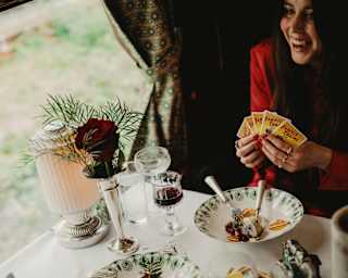 Two guests play cards as they enjoy bowls of desserts at a table with red wine and water, with a bud vase decoration.