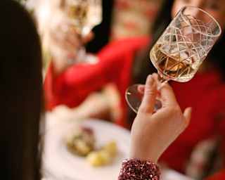 A woman with a purple sequined sleeve, mainly off-camera, raises a drink for a toast, mirrored by a friend in red, opposite.