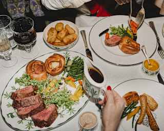 Diners enjoy roast beef, presented in slices with Yorkshire puddings, carrots, beans, potatoes and gravy, seen from above.
