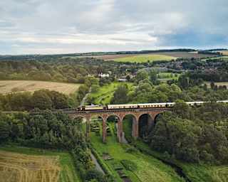 A birdseye view of the British Pullman crossing the arches of the Eynsford Viaduct, with glimpses of the village in the distance